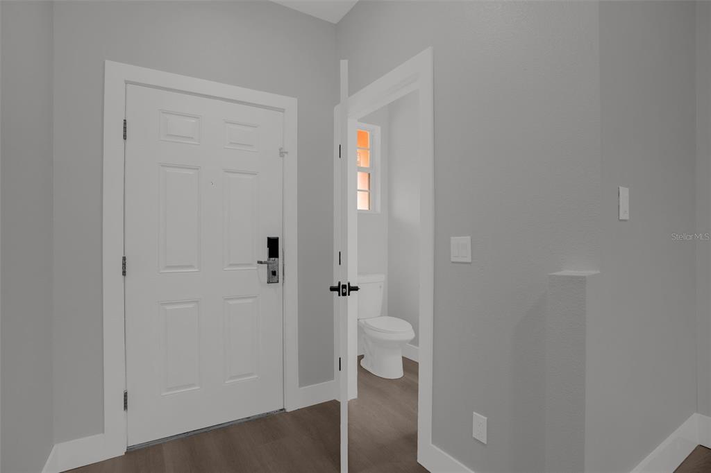 A white front door stands next to a small bathroom with a toilet and window — 815 ASSEMBLY COURT, KISSIMMEE, FL