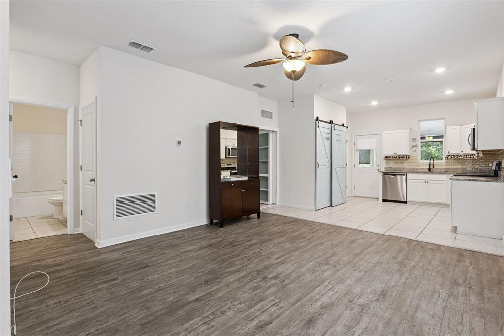 A kitchen with white cabinets and tile flooring opens into a living area with wood-look flooring — 2059 CADES COVE WAY, DELAND, FL
