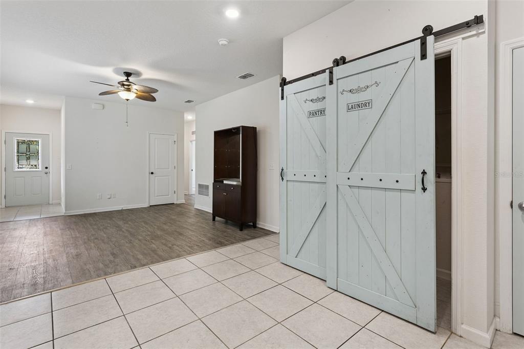 A living room with wood-look flooring transitions into a tiled kitchen area with white cabinets — 2059 CADES COVE WAY, DELAND, FL