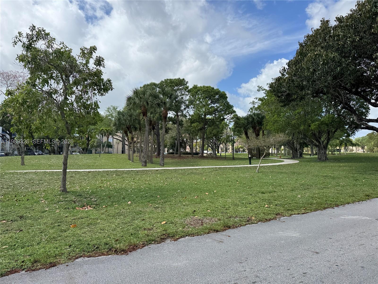 A paved path winds through a grassy park filled with various trees under a cloudy sky — 6301 N Fall Circle Dr # 213, Lauderhill FL 33319, LAUDERHILL, FL