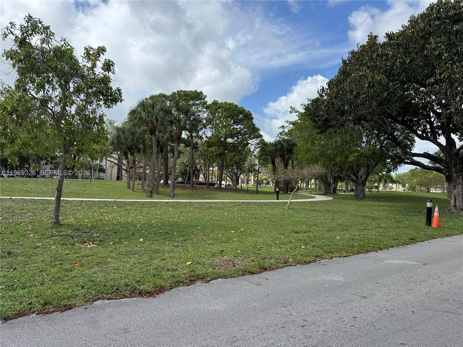 A paved path winds through a grassy park filled with various trees under a cloudy sky — 6301 N Fall Circle Dr # 213, Lauderhill FL 33319, LAUDERHILL, FL