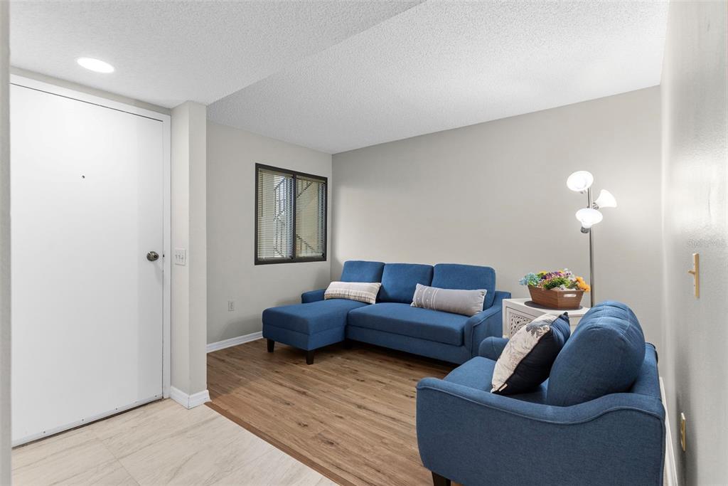 A living room with wood-look flooring features a brown sofa, recliner, and an adjacent dining area — 6035 SEA RANCH DRIVE UNIT 209, HUDSON, FL