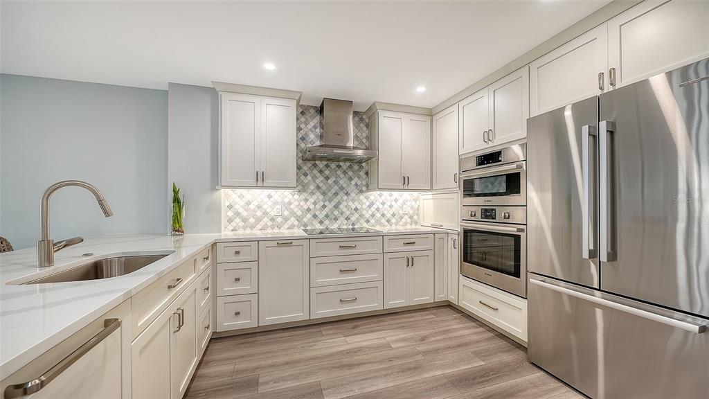 A modern kitchen features white cabinetry, stainless steel appliances, a tiled backsplash, and wood flooring — 5780 MIDNIGHT PASS ROAD UNIT 110, SARASOTA, FL