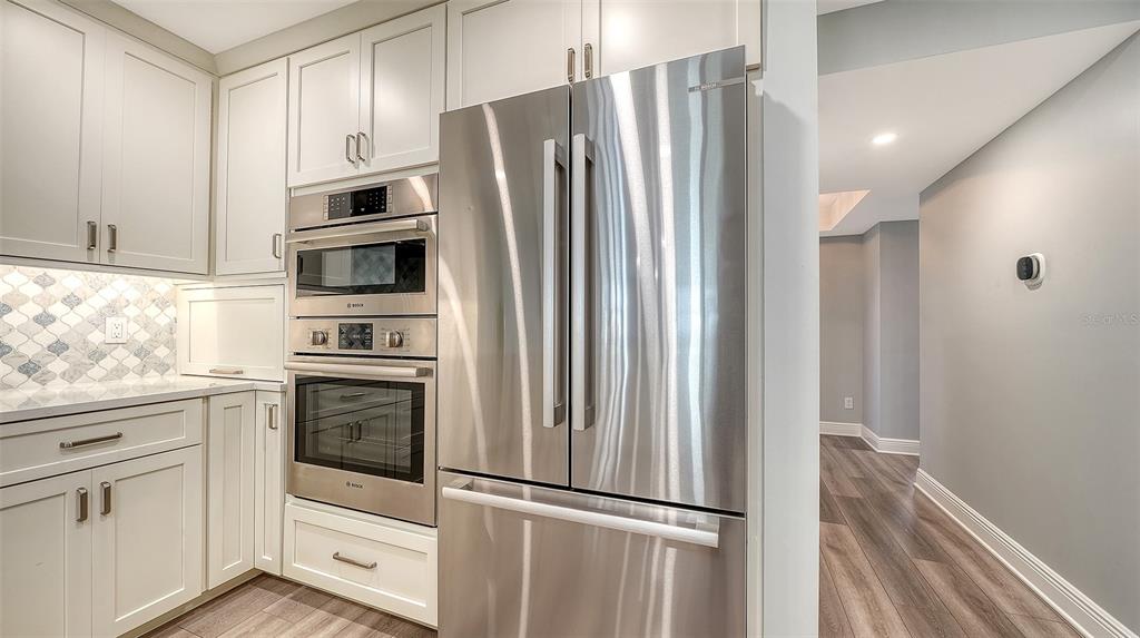 A modern kitchen features white cabinetry, stainless steel appliances, and a patterned tile backsplash — 5780 MIDNIGHT PASS ROAD UNIT 110, SARASOTA, FL