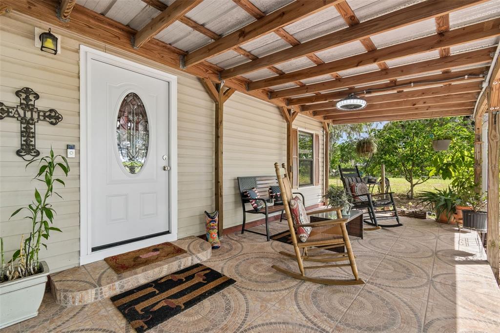 A covered porch with tiled flooring, rocking chairs, a bench, and a white front door — 17114 BRITTLE ROAD, BROOKSVILLE, FL