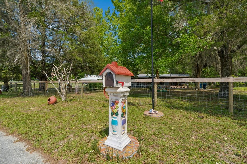 A decorative mailbox with a red roof stands on a tiled base in a yard — 17114 BRITTLE ROAD, BROOKSVILLE, FL