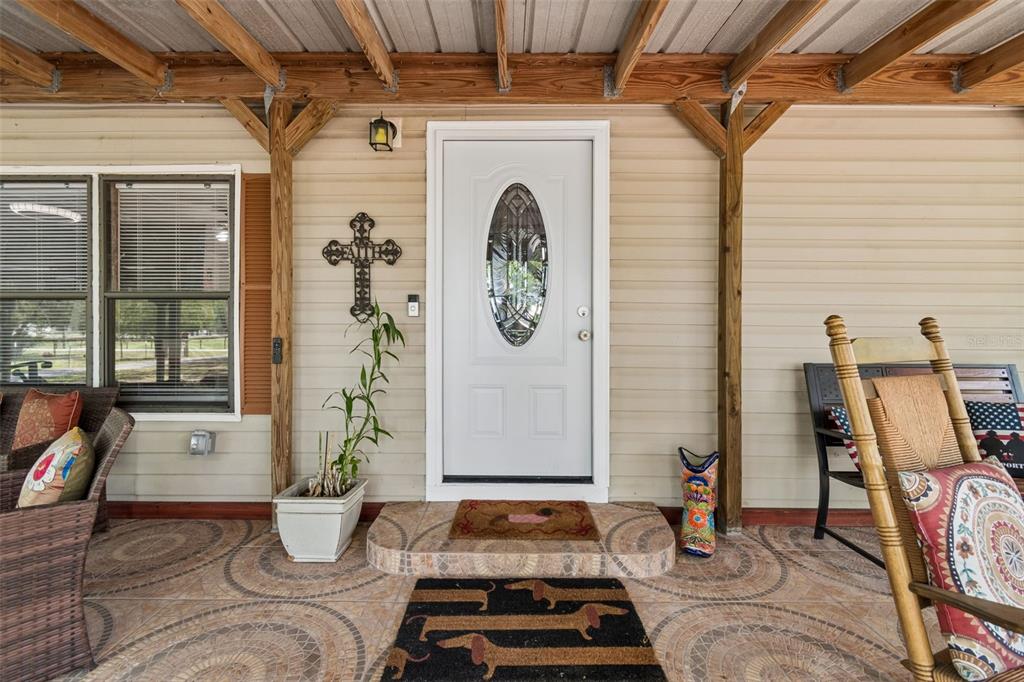 A covered front porch features a white door, tiled flooring, and two rocking chairs — 17114 BRITTLE ROAD, BROOKSVILLE, FL