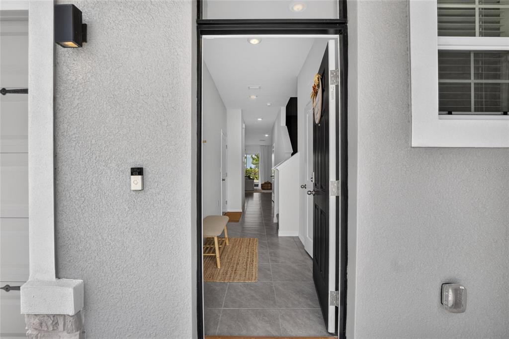 An open front door reveals a tiled entryway leading into a bright, modern home interior — 3816 SUNFLOWER FIELD PLACE, PLANT CITY, FL
