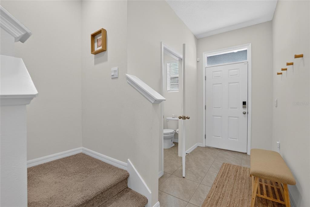 An entryway features a carpeted staircase, a tiled floor, a small bench, and a half bathroom — 3816 SUNFLOWER FIELD PLACE, PLANT CITY, FL
