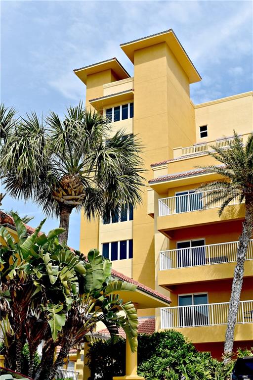 A multi-story yellow building features balconies and palm trees under a blue sky — 701 N ATLANTIC AVENUE W UNIT 401, NEW SMYRNA BEACH, FL