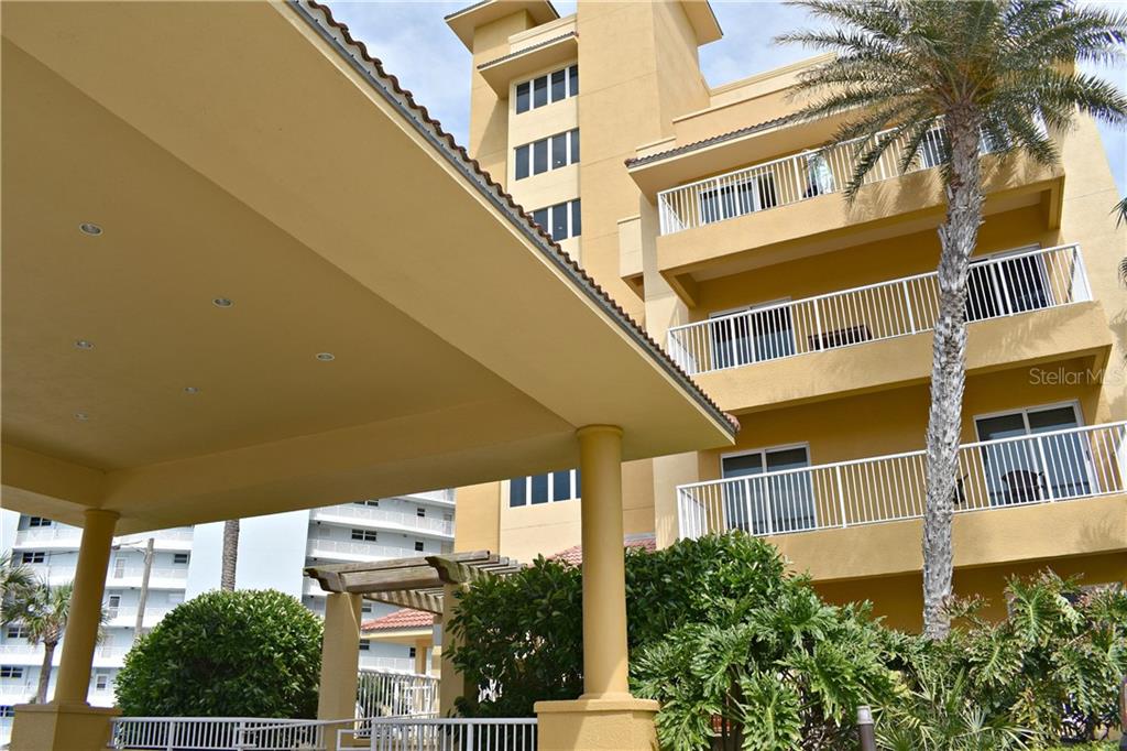 A low-angle view of a multi-story yellow building with balconies and a covered entrance — 701 N ATLANTIC AVENUE W UNIT 401, NEW SMYRNA BEACH, FL