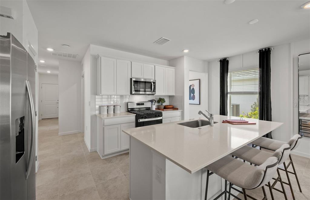A modern kitchen features white cabinets, stainless steel appliances, a quartz island, and tile flooring — 817 BALLEBY TRAIL, BRADENTON, FL