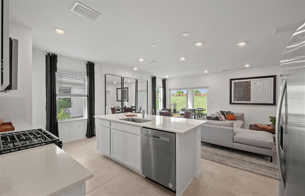 A modern kitchen with white cabinets and quartz countertops opens into a living and dining area — 817 BALLEBY TRAIL, BRADENTON, FL
