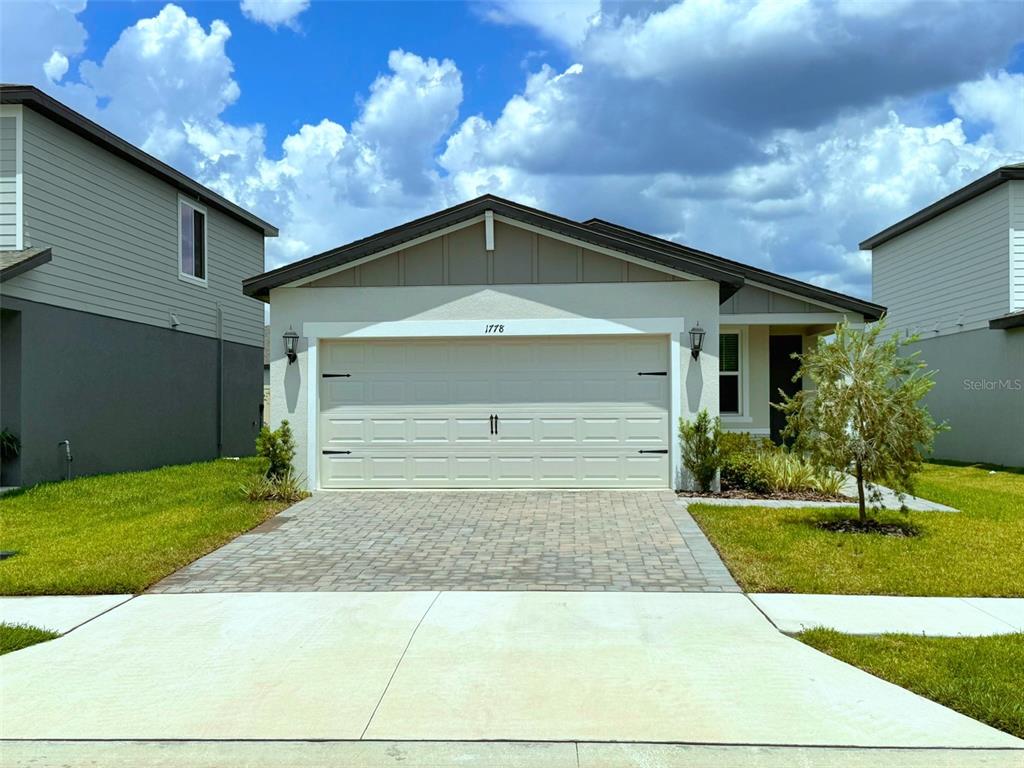 A single-story house with a beige garage, stucco exterior, and a paved driveway — 1778 BREKEY WAY, ZEPHYRHILLS, FL