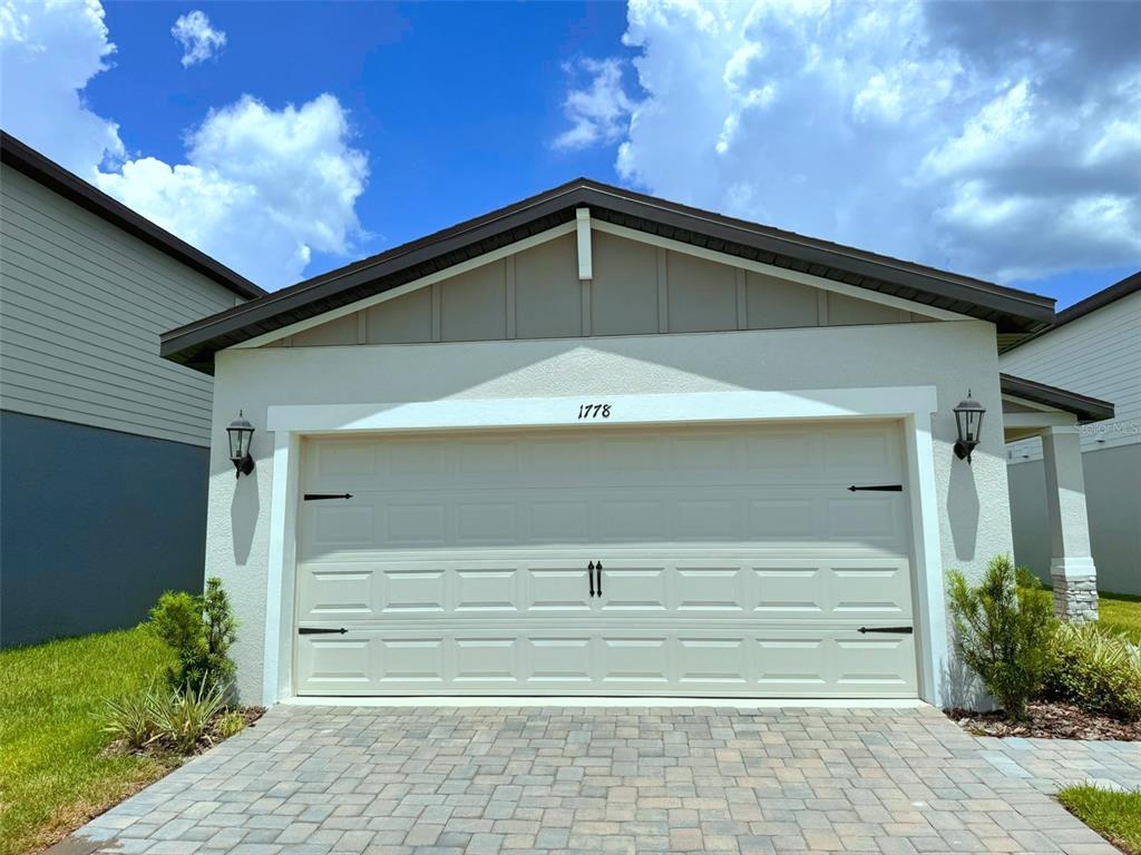A beige garage door with decorative hardware is centered on the front of a house — 1778 BREKEY WAY, ZEPHYRHILLS, FL