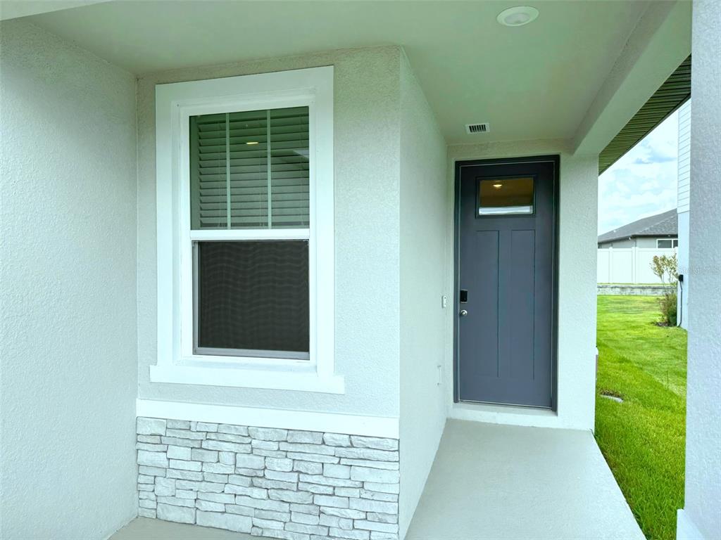 A covered entryway features a gray front door, a single window, and stone veneer siding — 1778 BREKEY WAY, ZEPHYRHILLS, FL