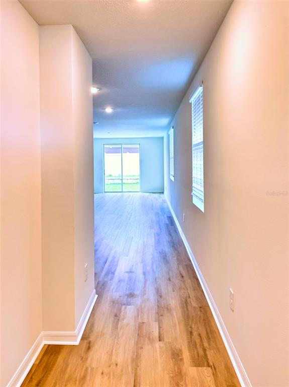 A hallway with light wood-look flooring leads to an open living area with sliding glass doors — 1778 BREKEY WAY, ZEPHYRHILLS, FL
