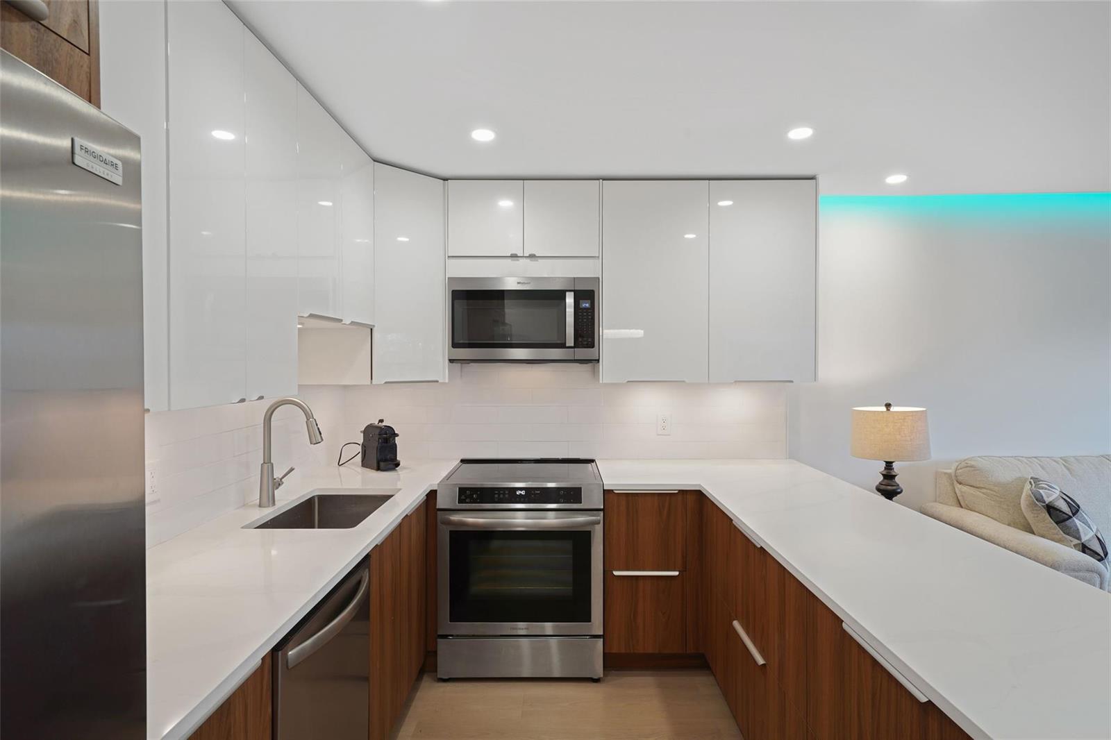 A modern kitchen features white glossy upper cabinets, wood-grain lower cabinets, and white quartz countertops — 3034 Berkshire B # 3034, Deerfield Beach FL 33442, DEERFIELD BEACH, FL