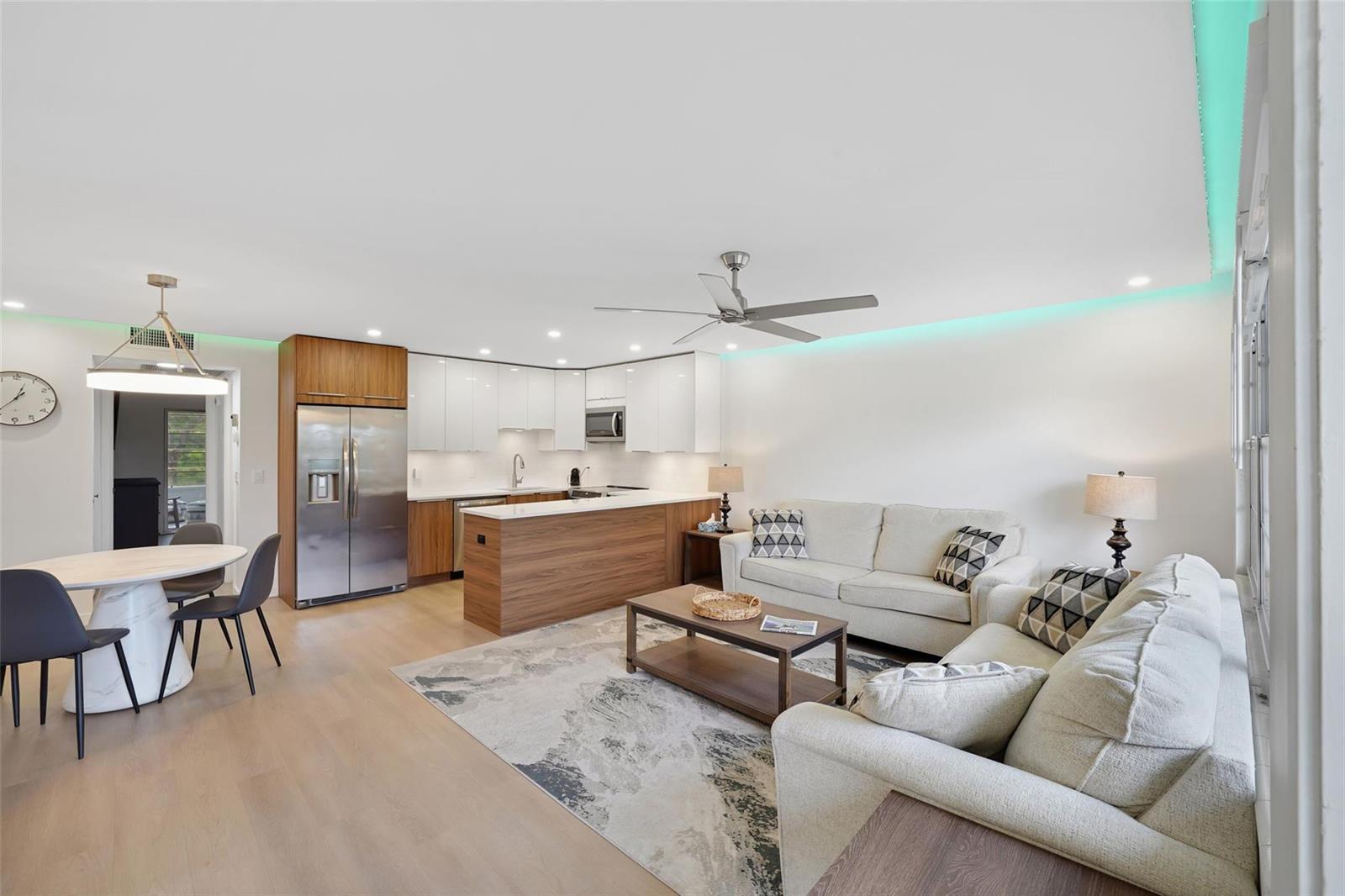 An open-concept living room and kitchen featuring white cabinetry, wood accents, and light flooring — 3034 Berkshire B # 3034, Deerfield Beach FL 33442, DEERFIELD BEACH, FL