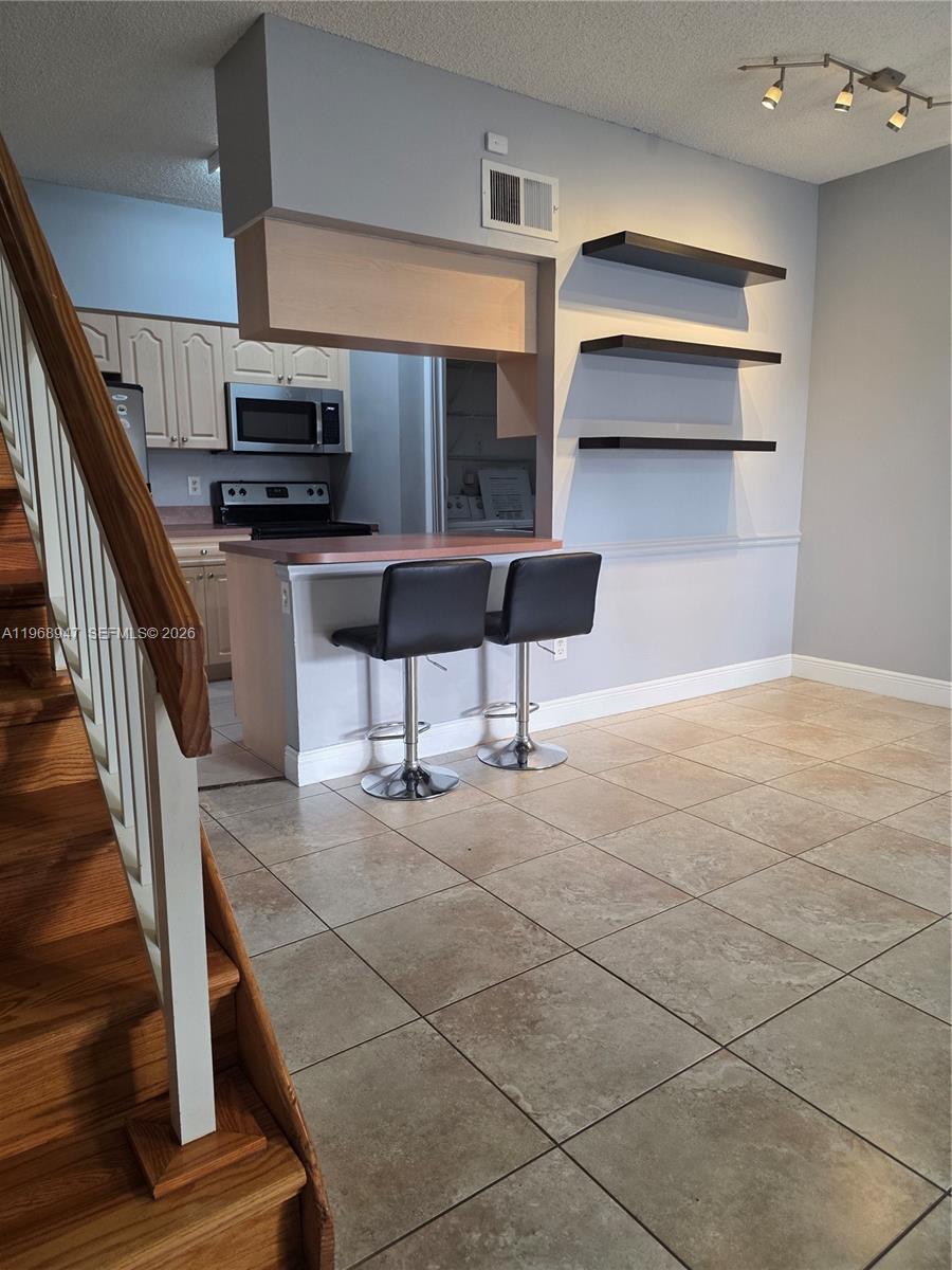 A kitchen with a breakfast bar, two stools, and wall-mounted shelves sits beside a staircase — 18316 NW 68th Ave # C, Hialeah FL 33015, HIALEAH, FL