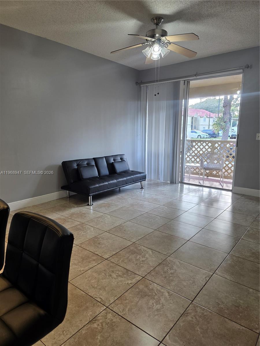 A living room features light gray walls, beige tile flooring, a black futon, and a balcony — 18316 NW 68th Ave # C, Hialeah FL 33015, HIALEAH, FL