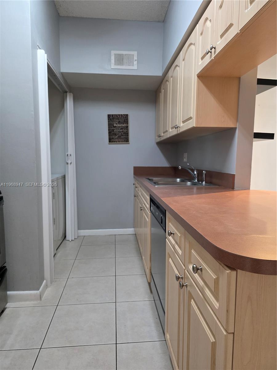 A kitchen features light wood cabinets, a reddish-brown countertop, and a stainless steel dishwasher — 18316 NW 68th Ave # C, Hialeah FL 33015, HIALEAH, FL