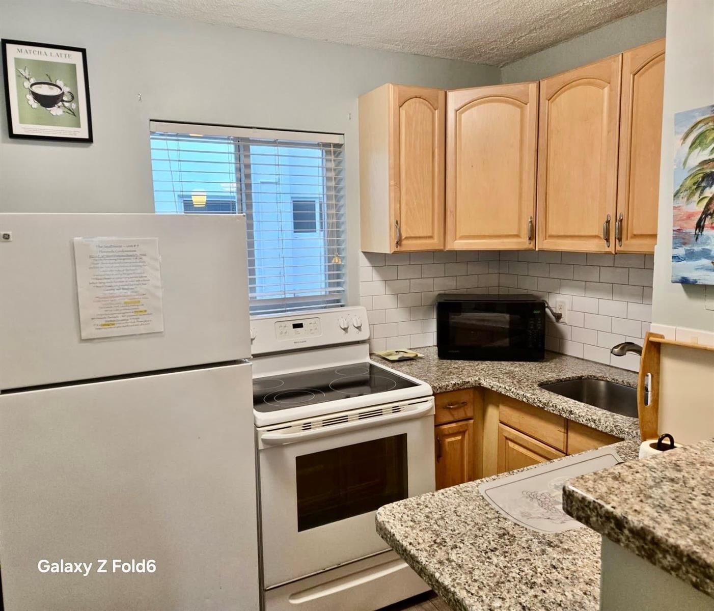A kitchen features light wood cabinets, granite countertops, white appliances, and a subway tile backsplash — 3225 NE 16th Street # 9A, Pompano Beach FL 33062, POMPANO BEACH, FL
