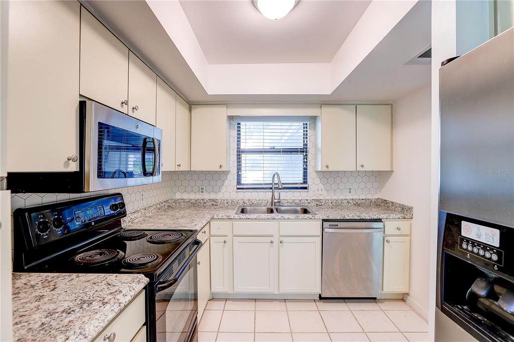 A kitchen features white cabinets, granite countertops, stainless steel appliances, and a hexagonal tile backsplash — 6643 TRAIL RIDGE DRIVE UNIT 00, LAKELAND, FL
