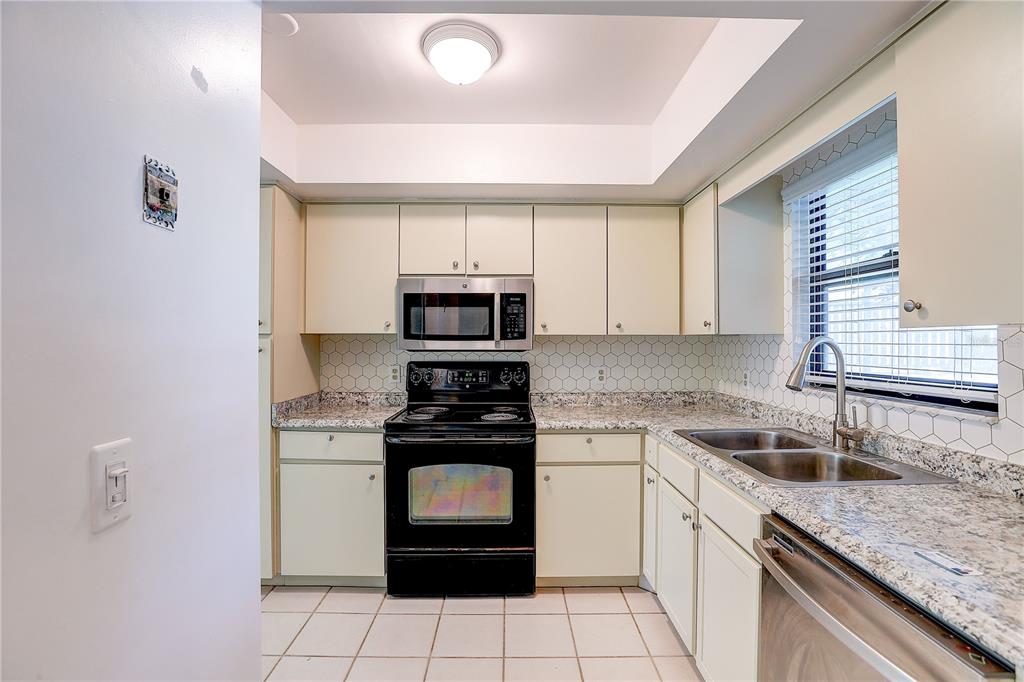 A kitchen features off-white cabinets, granite countertops, a black stove, and a white tile backsplash — 6643 TRAIL RIDGE DRIVE UNIT 00, LAKELAND, FL
