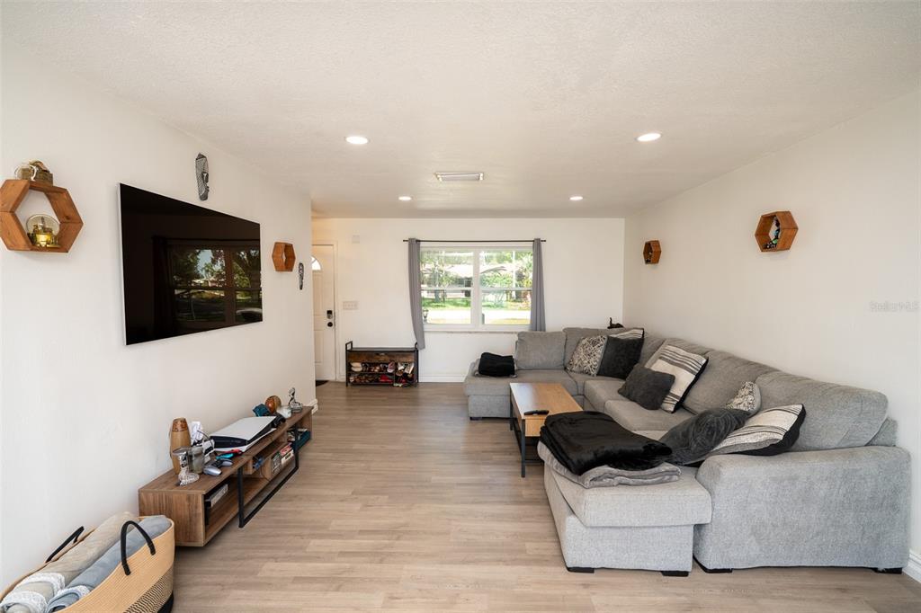 A living room features light wood-look flooring, a large gray sectional sofa, and a wall-mounted television — 2131 HAINLIN COURT, DELTONA, FL