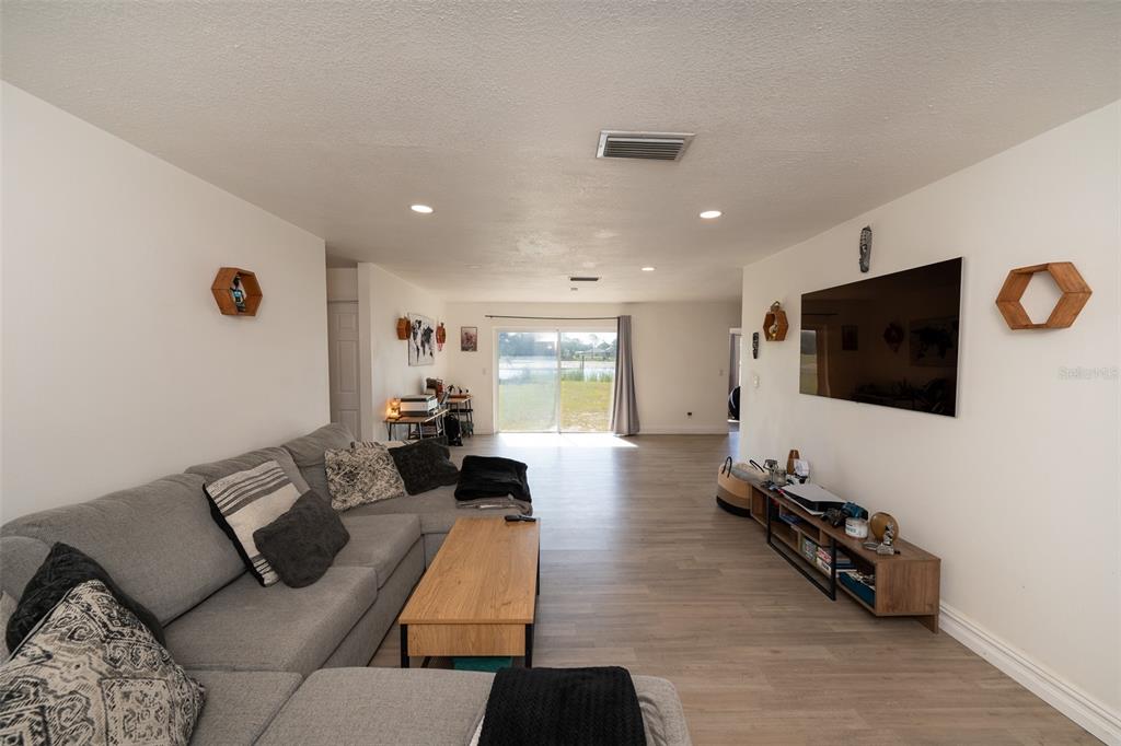 A living room with light wood-look flooring, a gray sectional sofa, and a wall-mounted television — 2131 HAINLIN COURT, DELTONA, FL