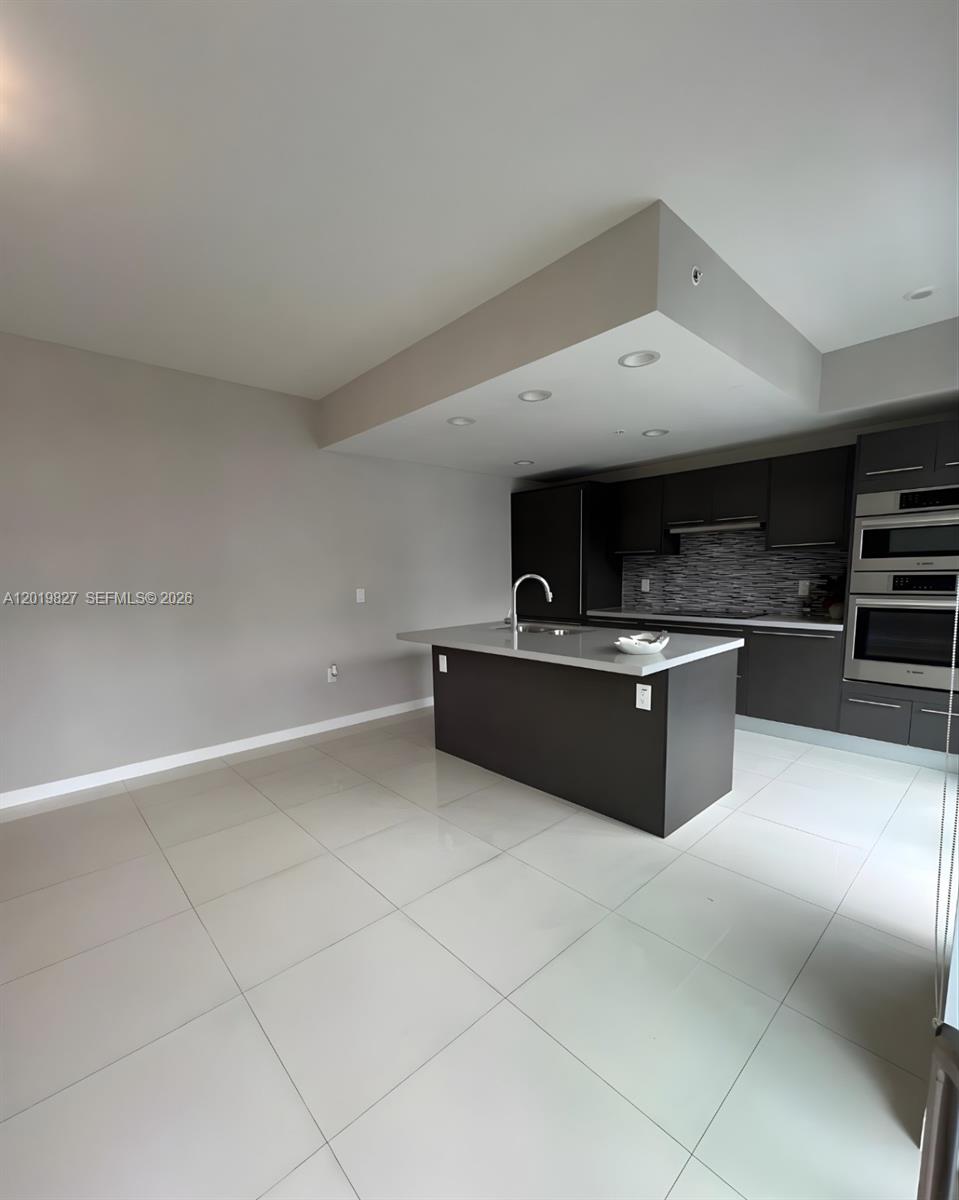 A modern kitchen features dark cabinetry, a central island with a sink, and light tile flooring — 7875 NW 107th Ave # 412, Doral FL 33178, DORAL, FL