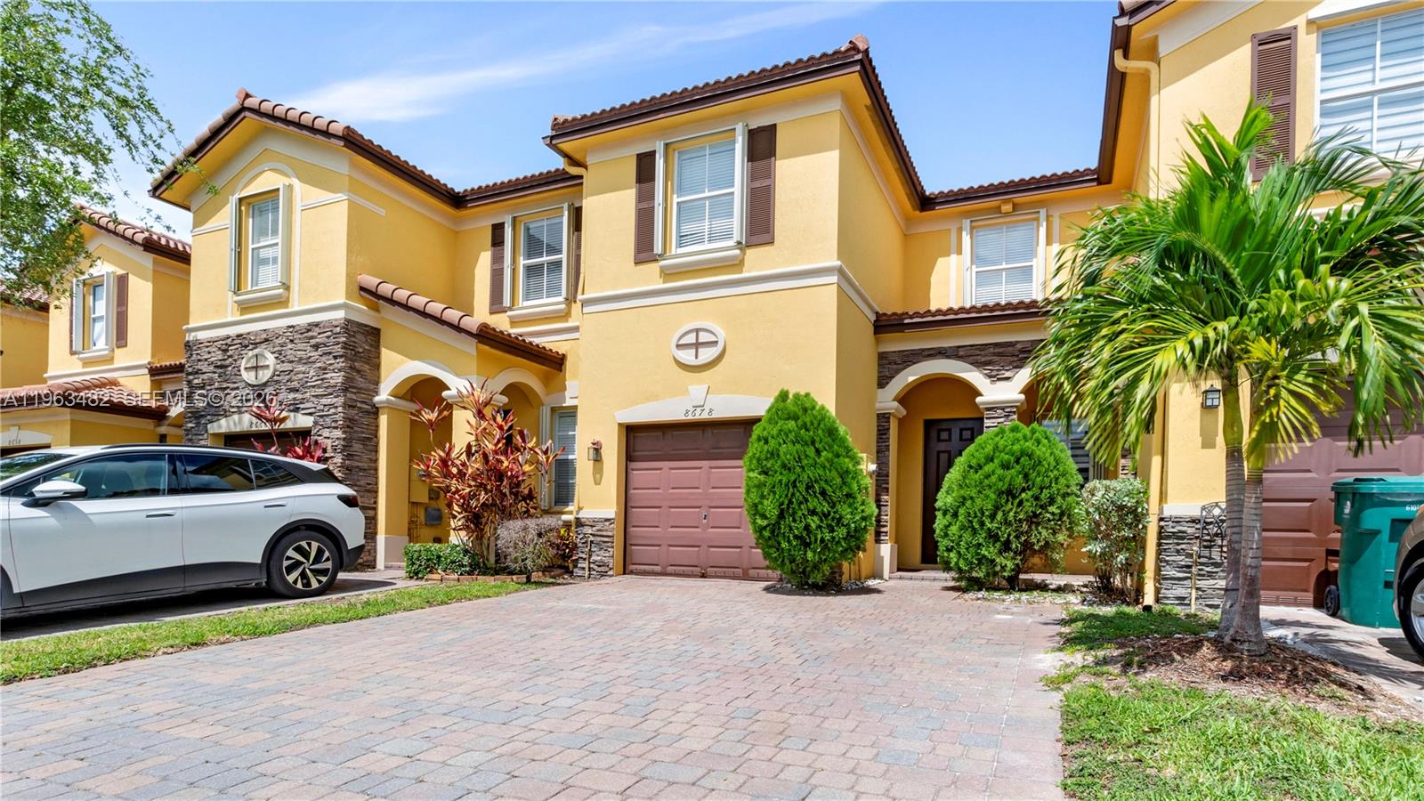A yellow two-story townhouse with a stone facade, brown garage door, and paved driveway — 8678 NW 113th Ct, Doral FL 33178, DORAL, FL