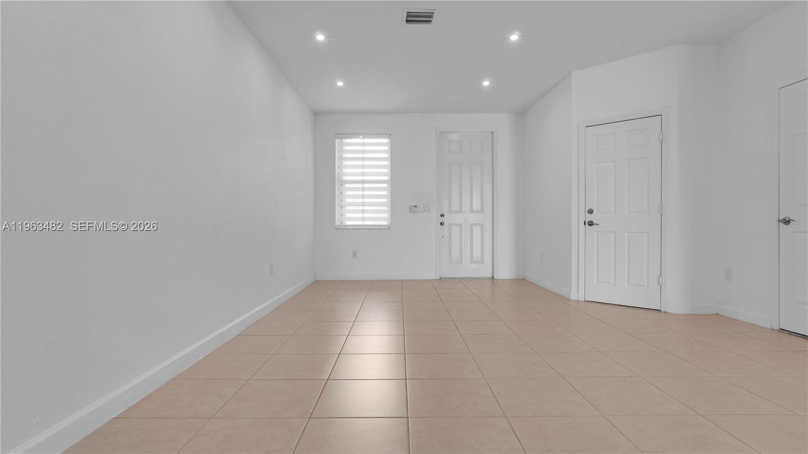 A bright, empty room features white walls, light-colored tile flooring, and recessed ceiling lighting — 8678 NW 113th Ct, Doral FL 33178, DORAL, FL