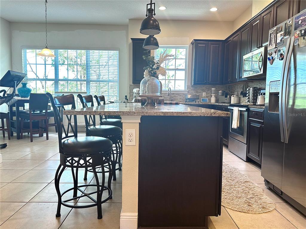 A kitchen features dark wood cabinetry, a granite-topped island with bar stools, and tile flooring — 1220 LOBELIA DRIVE, LAKE MARY, FL