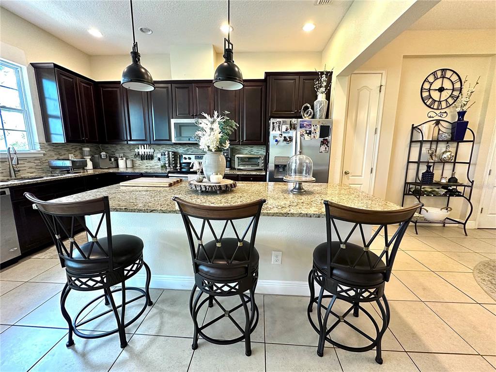 A kitchen features dark wood cabinets, granite countertops, a central island, and three bar stools — 1220 LOBELIA DRIVE, LAKE MARY, FL