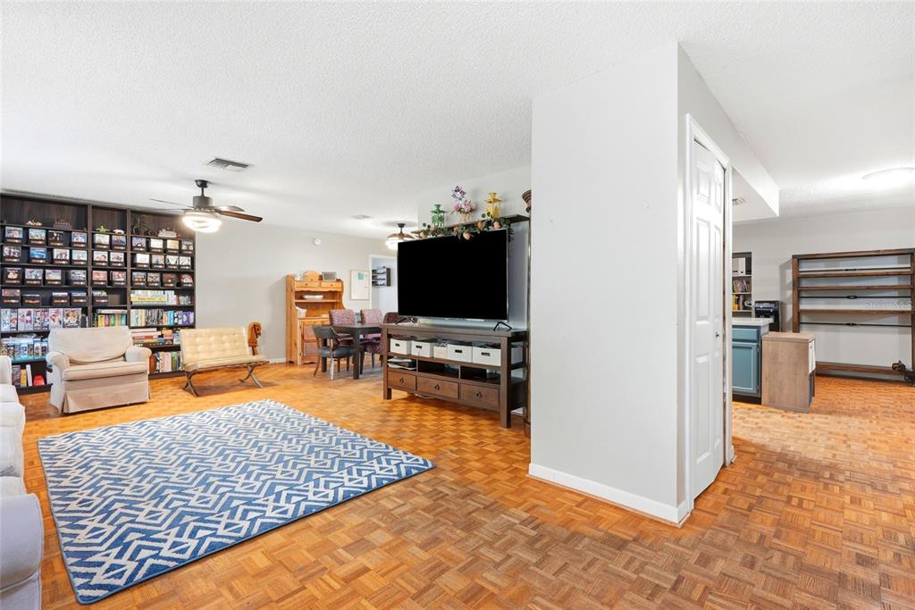 A living room with parquet wood flooring, a large bookshelf, and a television console — 6300 86TH AVENUE N, PINELLAS PARK, FL