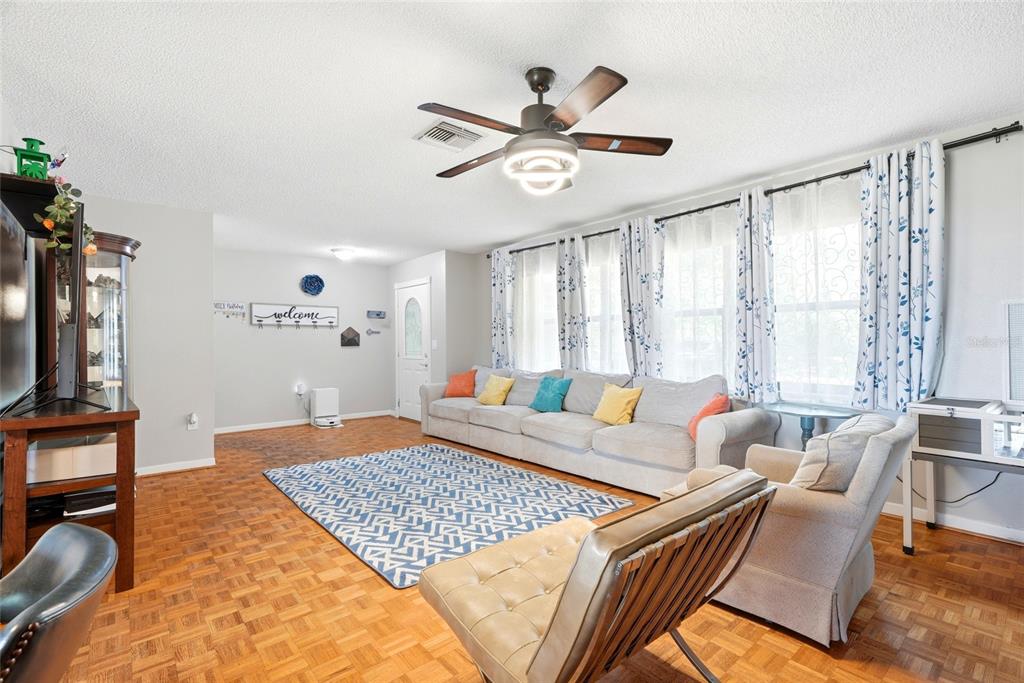 A living room features parquet wood flooring, a ceiling fan, and a large gray sectional sofa — 6300 86TH AVENUE N, PINELLAS PARK, FL