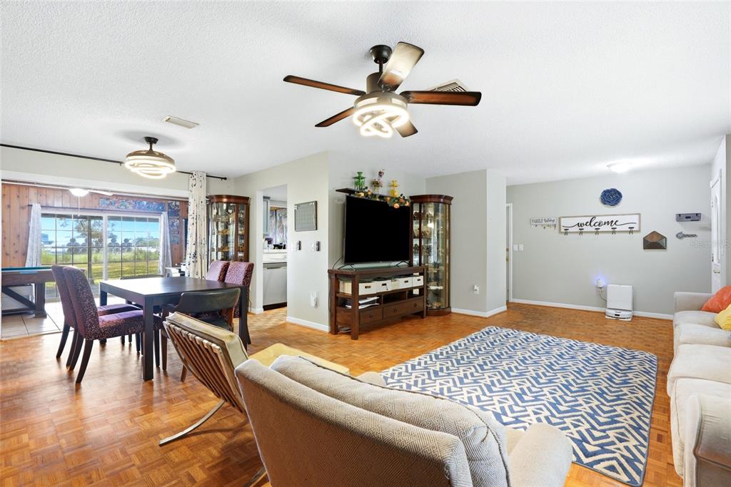 A living and dining area features parquet wood flooring, a ceiling fan, and a television — 6300 86TH AVENUE N, PINELLAS PARK, FL