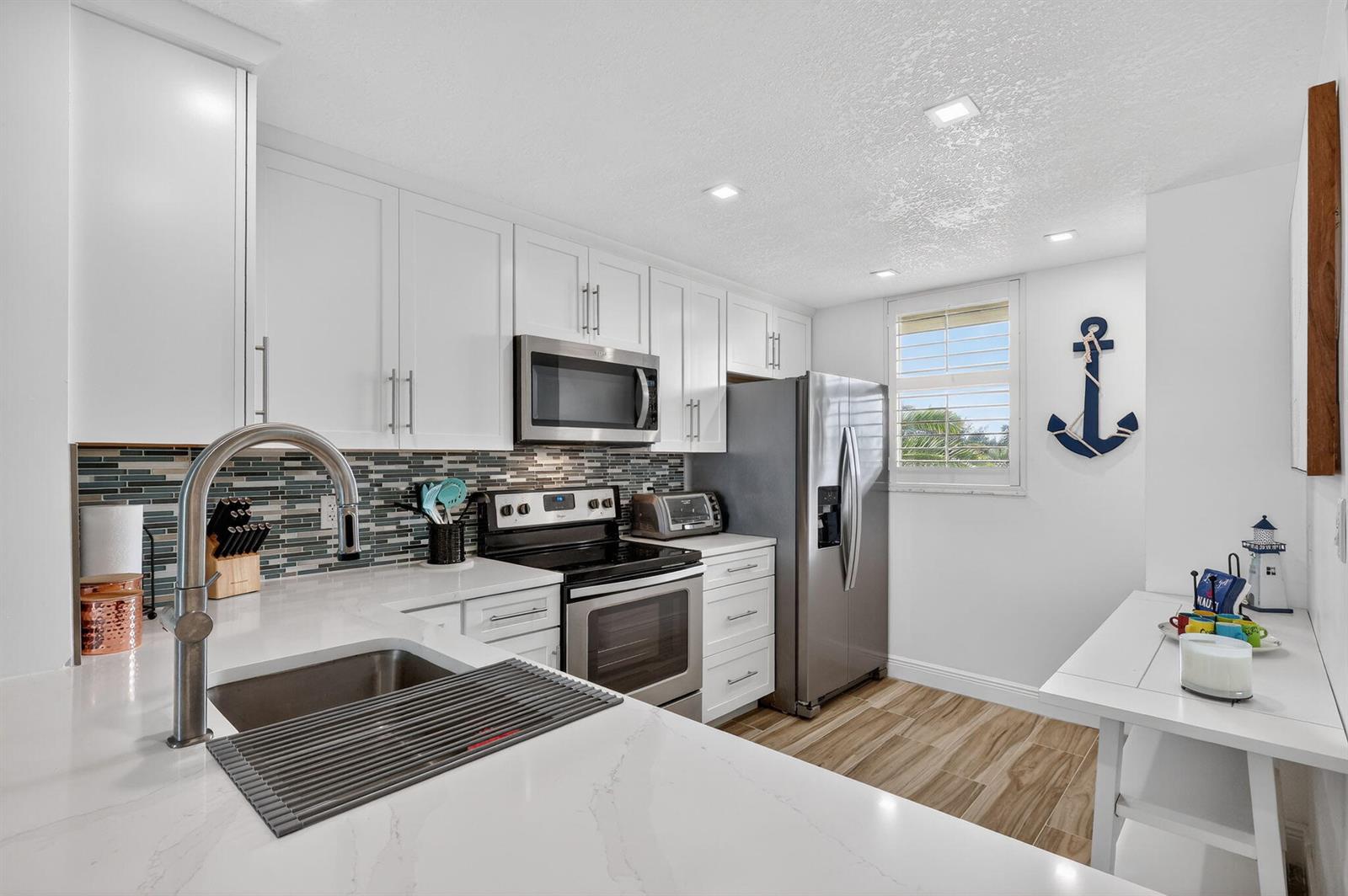 A modern kitchen features white cabinets, stainless steel appliances, a tiled backsplash, and nautical decor — 9940 S Ocean Drive # 202, Jensen Beach FL 34957, JENSEN BEACH, FL