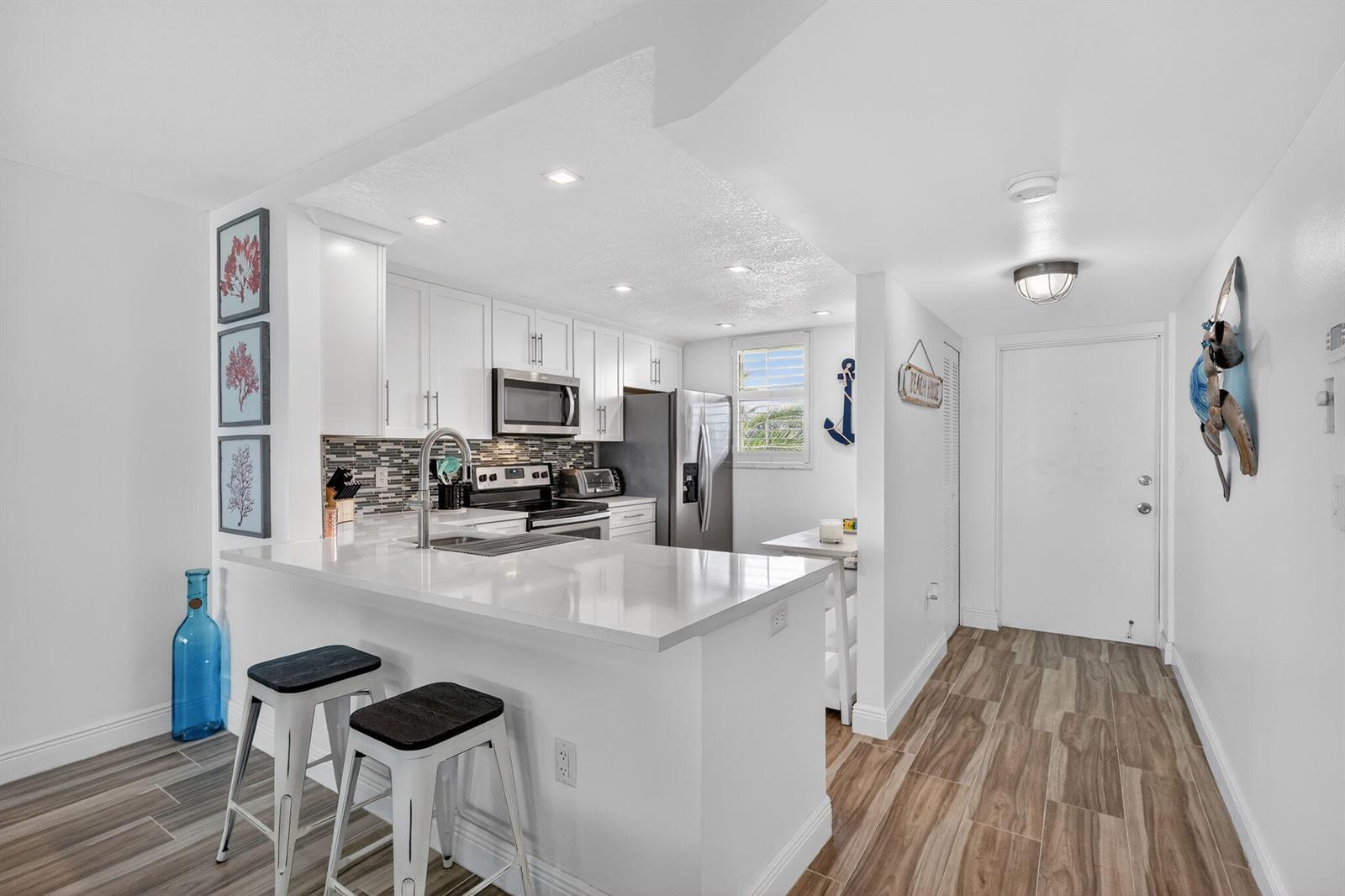 A modern kitchen features white cabinets, quartz countertops, a breakfast bar, and wood-look tile flooring — 9940 S Ocean Drive # 202, Jensen Beach FL 34957, JENSEN BEACH, FL