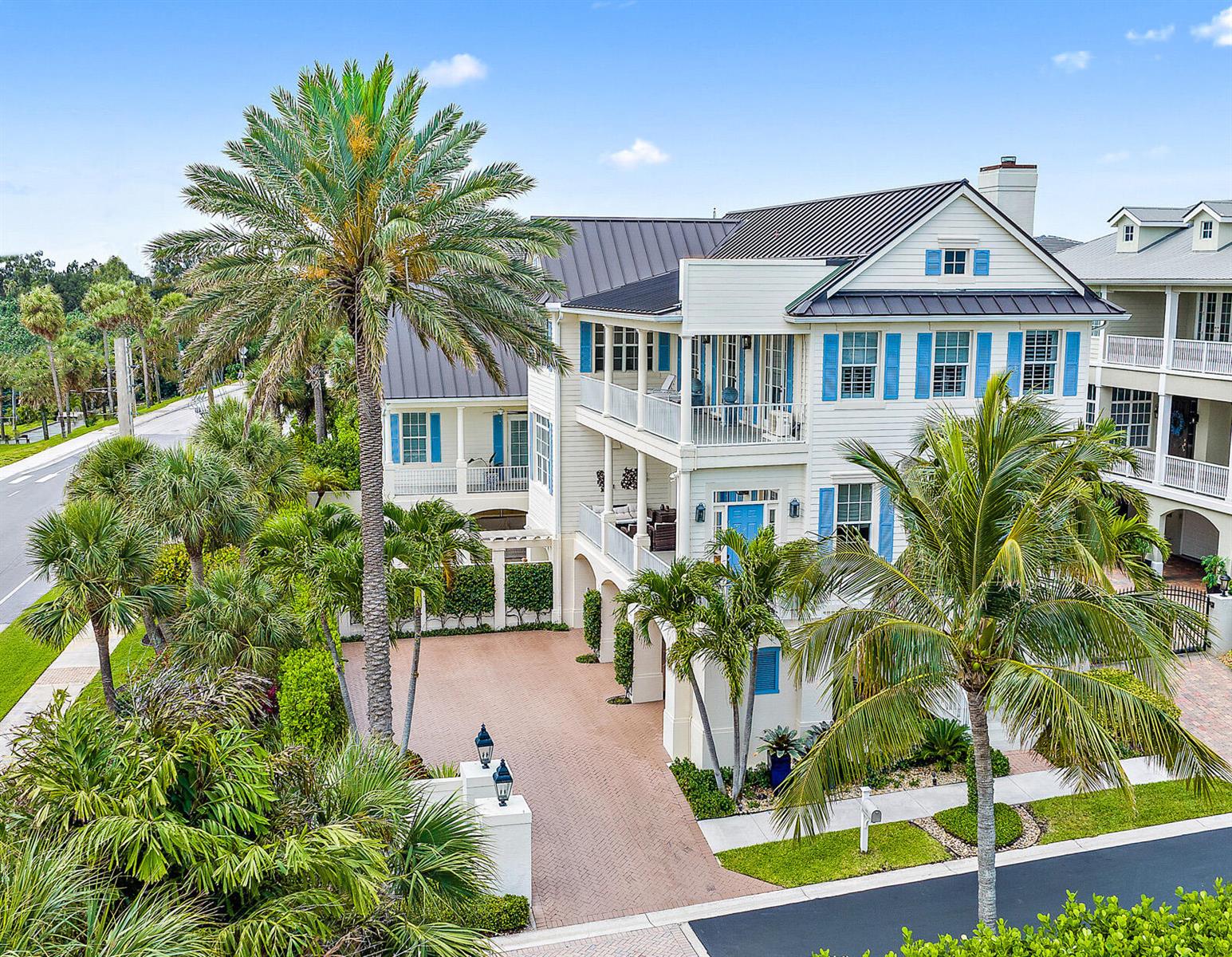 An exterior view of a multi-story coastal home with blue shutters and a paved driveway — 410 Old Towne Lane, Juno Beach FL 33408, JUNO BEACH, FL
