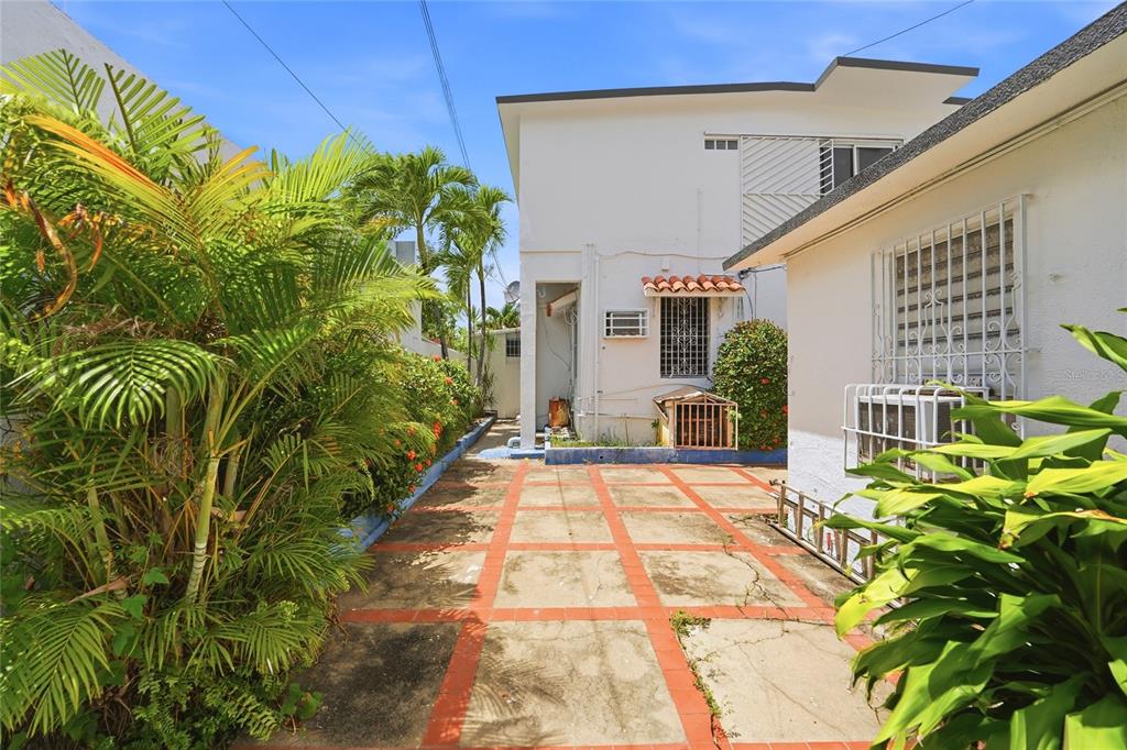 A paved outdoor patio area sits between two white buildings surrounded by lush tropical plants — 2202 GENERAL PATTON, SAN JUAN, PR