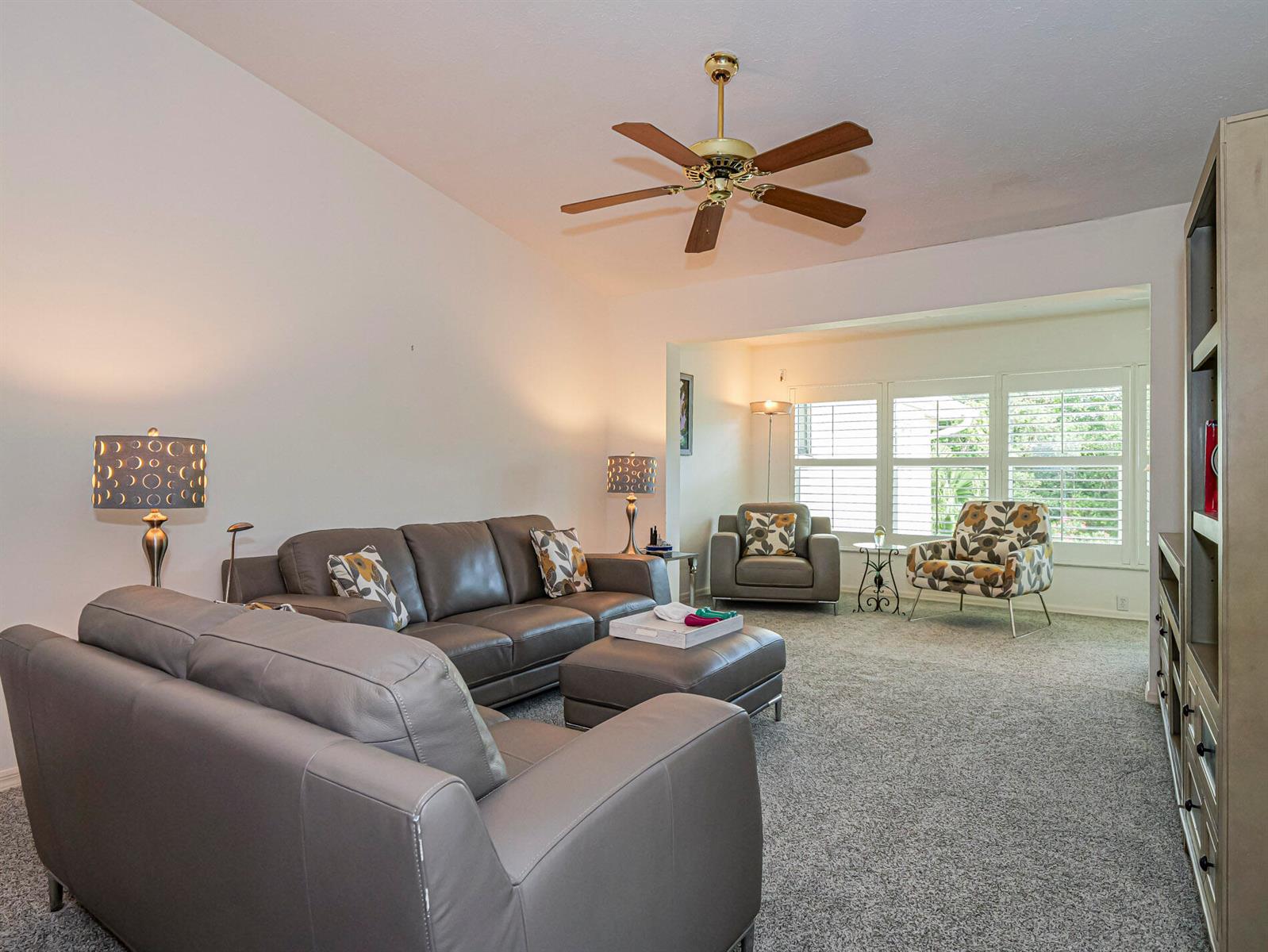 A living room features gray leather furniture, a ceiling fan, and a large window — 700 Lake Orchid Circle # 209, Vero Beach FL 32962, VERO BEACH, FL