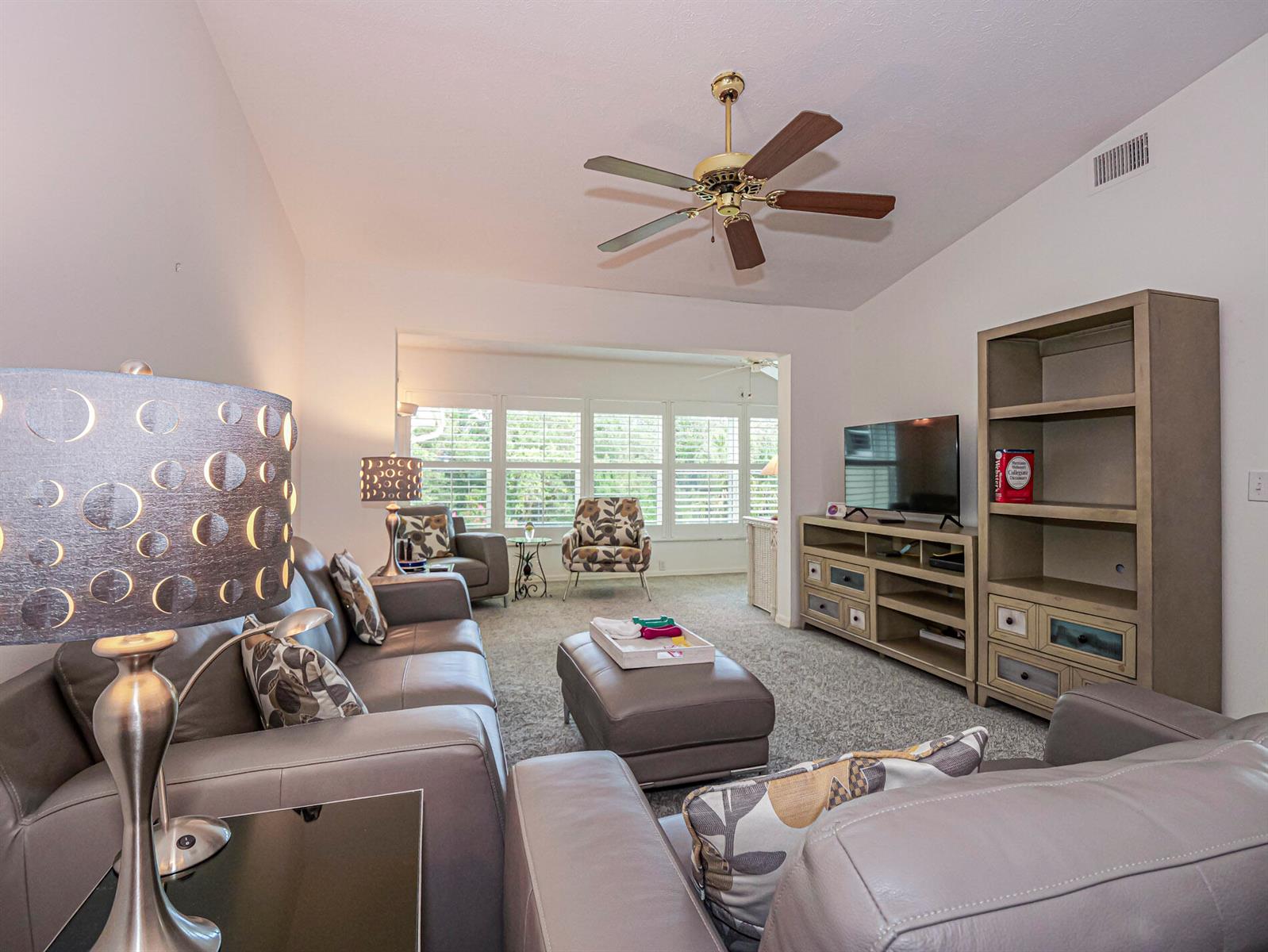 A living room features gray leather furniture, a ceiling fan, and a television console unit — 700 Lake Orchid Circle # 209, Vero Beach FL 32962, VERO BEACH, FL