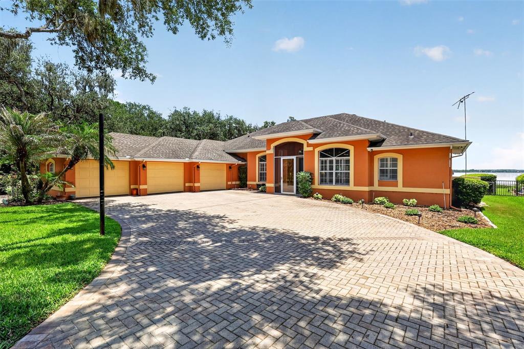 A single-story orange house with a three-car garage and a paved driveway — 29742 SQUIRREL POINT ROAD, TAVARES, FL