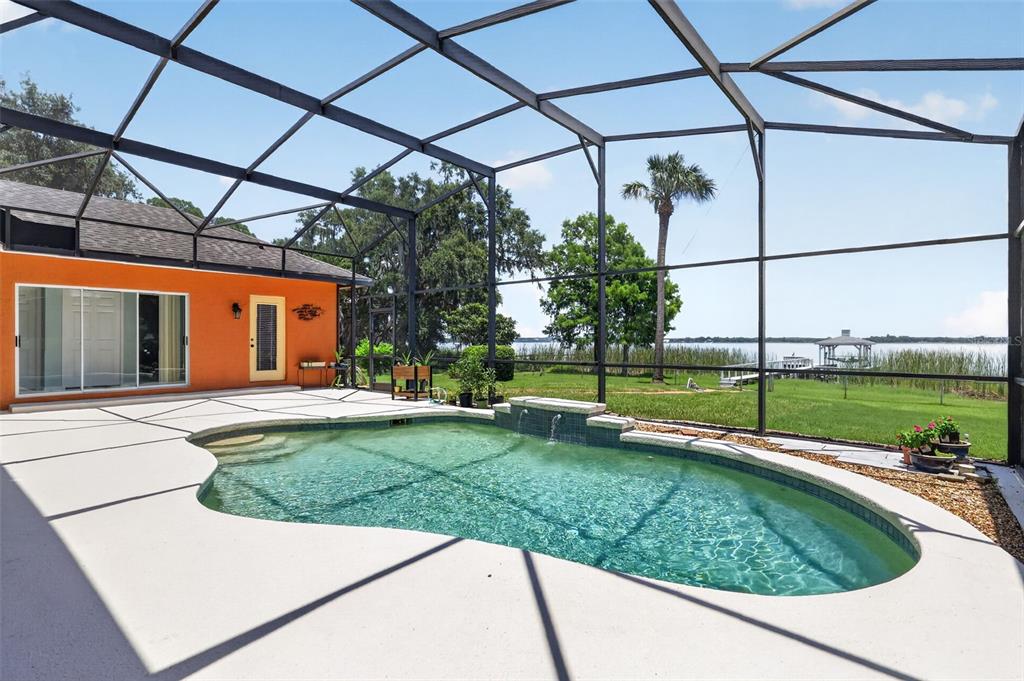 A screened-in patio features a swimming pool with a water feature overlooking a lake — 29742 SQUIRREL POINT ROAD, TAVARES, FL