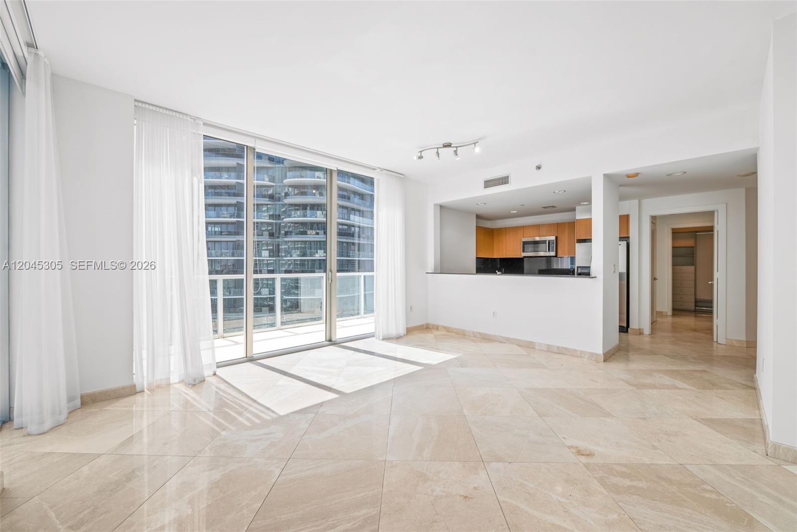 An empty living room features light-colored tile flooring, a kitchen pass-through, and a balcony view — 1050 Brickell Ave # 3314, Miami FL 33131, MIAMI, FL