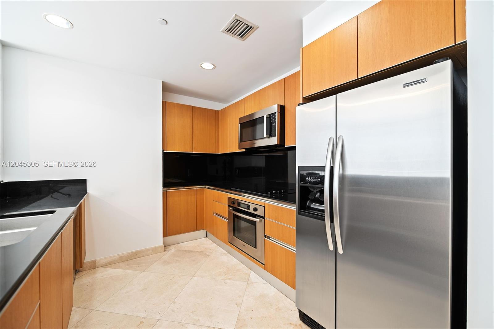 A kitchen features light wood cabinets, black countertops, stainless steel appliances, and tile flooring — 1050 Brickell Ave # 3314, Miami FL 33131, MIAMI, FL