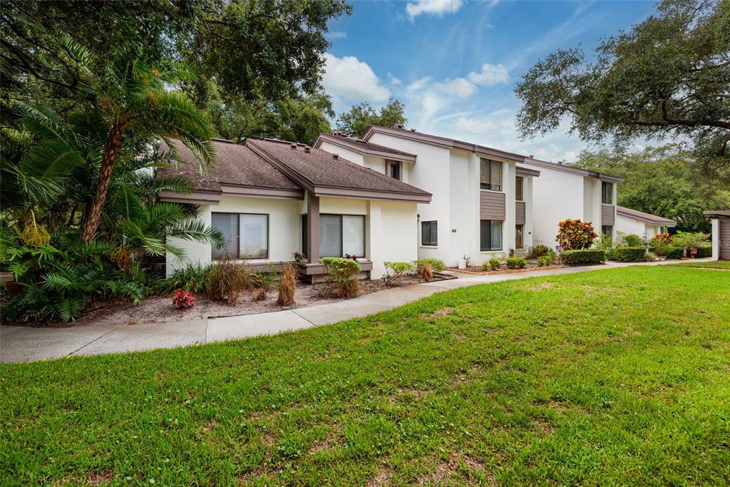 A multi-story residential building with white stucco walls, brown trim, and a landscaped front yard — 1750 LAKE CYPRESS DRIVE UNIT 1002, SAFETY HARBOR, FL